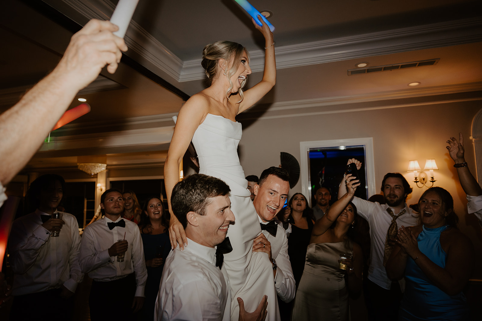 Bride waves a glow stick while being carried on shoulders during a high-energy reception dance.